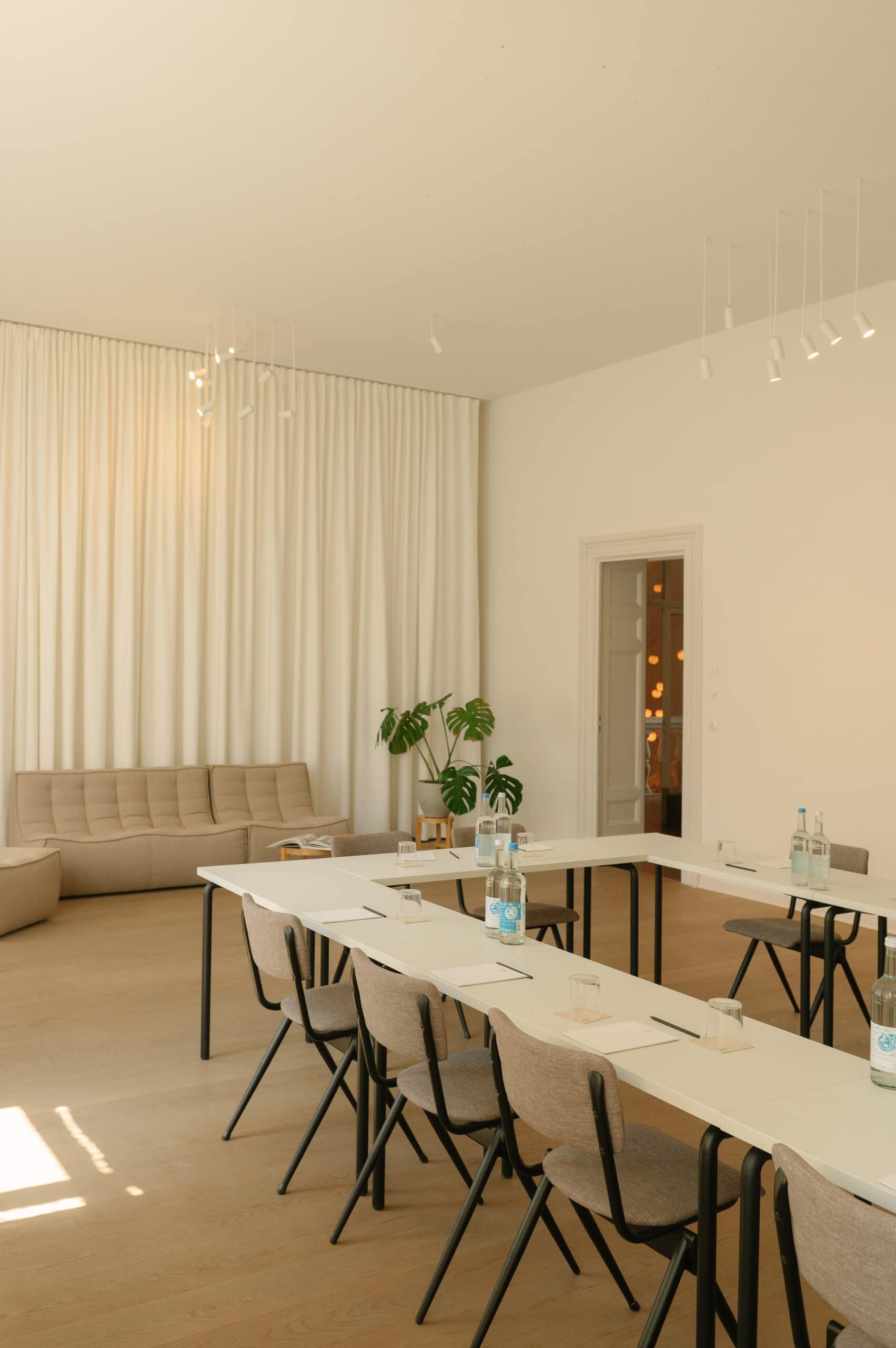 Bright conference room with beige sofa, white tables, and chairs, and green plant decor.