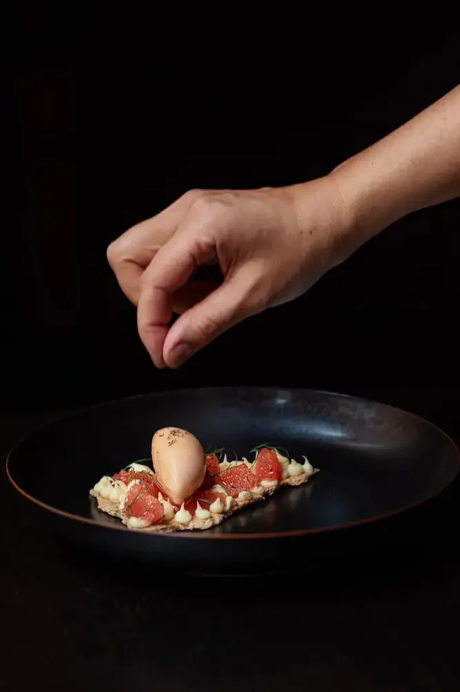 Hand platziert Ei auf Dessert mit Erdbeeren auf schwarzem Teller.