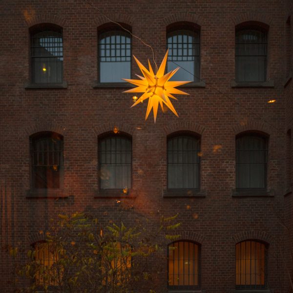 Hängende Weihnachtsstern-Lampe vor rotem Backstein-Gebäude.