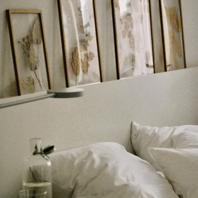 Schlafzimmer mit weißen Bettwäsche und Wanddekoration aus getrockneten Blumen.